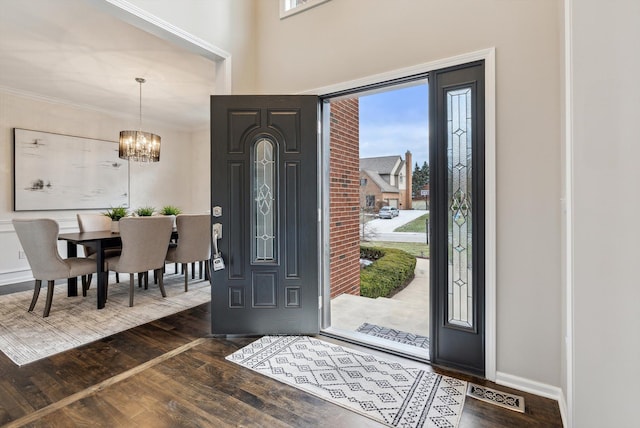 foyer entrance featuring crown molding, dark wood-type flooring, and a chandelier