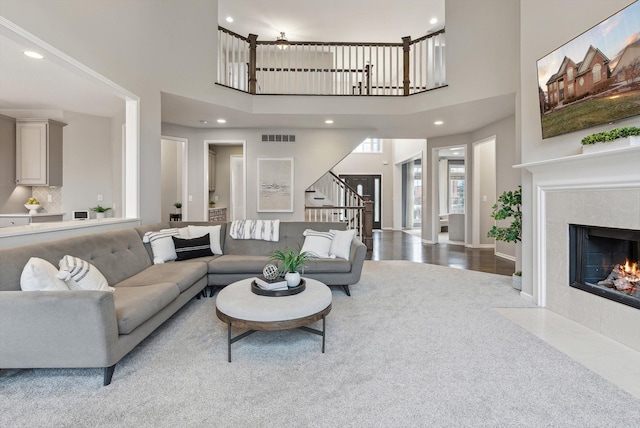 carpeted living room with a tiled fireplace and a high ceiling