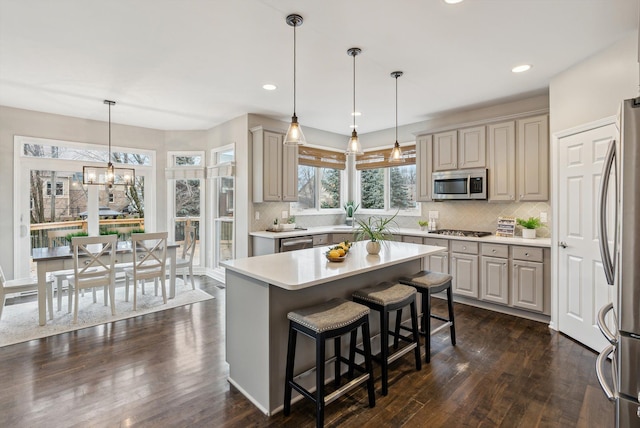 kitchen with decorative backsplash, appliances with stainless steel finishes, an inviting chandelier, a kitchen island, and hanging light fixtures