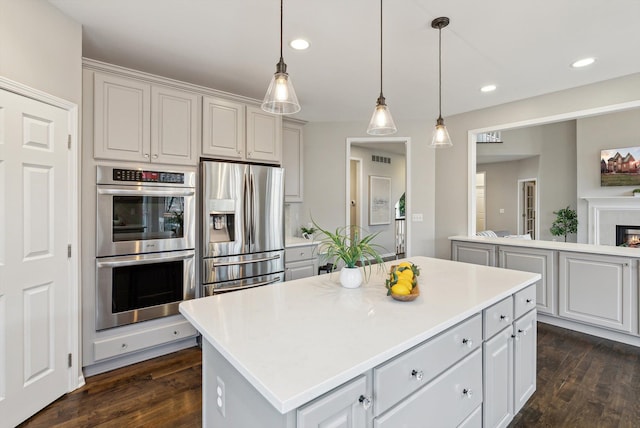 kitchen with dark wood-type flooring, a kitchen island, pendant lighting, white cabinets, and appliances with stainless steel finishes