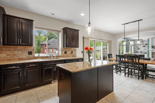 kitchen with backsplash, dark brown cabinetry, decorative light fixtures, a kitchen island, and plenty of natural light