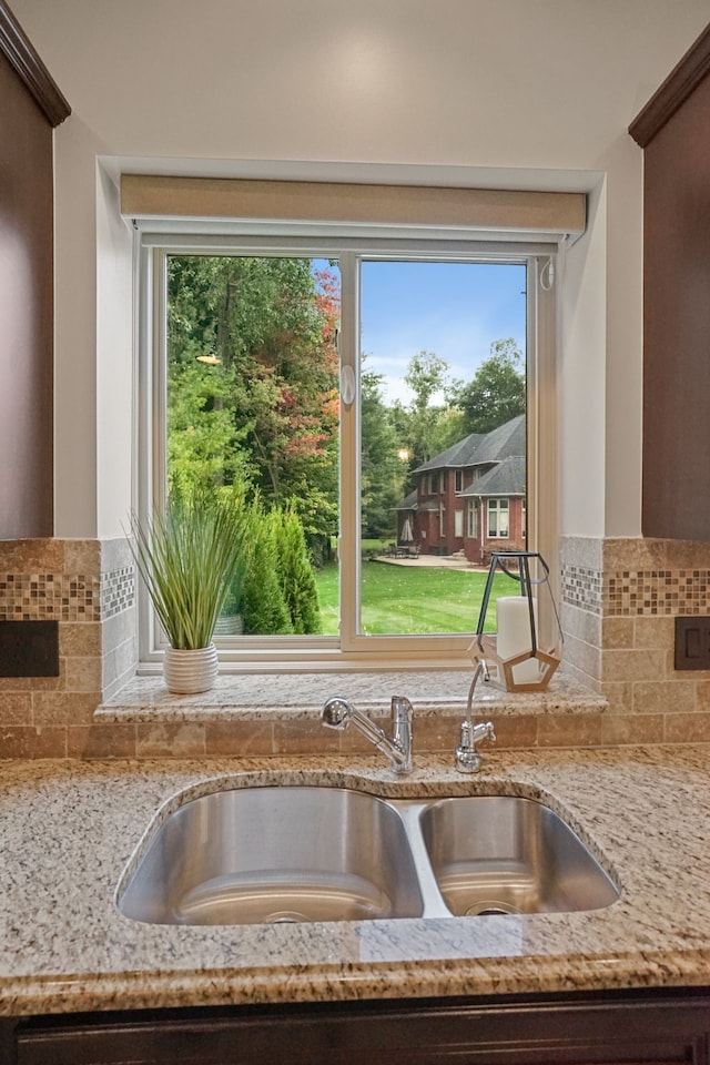 room details with light stone countertops, backsplash, dark brown cabinetry, and sink