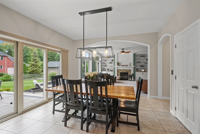 tiled dining space with ceiling fan, a stone fireplace, and built in features