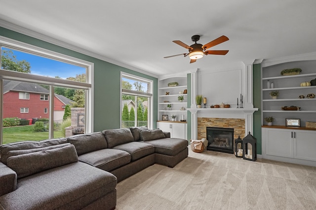 carpeted living room featuring built in shelves, ceiling fan, crown molding, and a fireplace