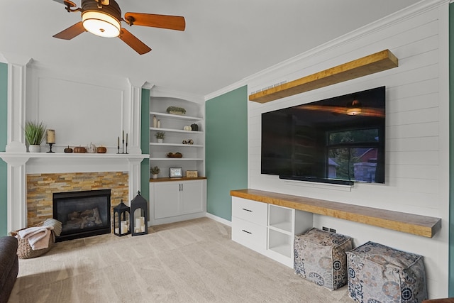 living room featuring ceiling fan, built in features, a fireplace, ornamental molding, and light colored carpet