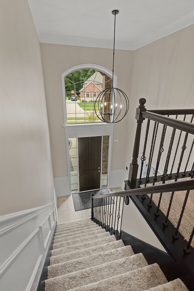 staircase with tile patterned floors, ornamental molding, and an inviting chandelier