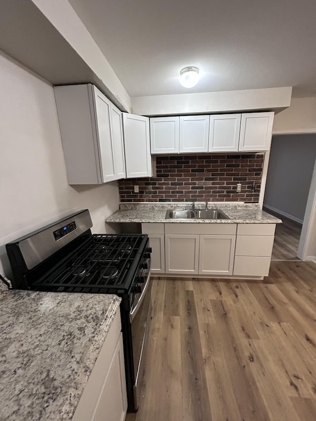 kitchen featuring backsplash, stainless steel gas range, sink, white cabinets, and light hardwood / wood-style floors