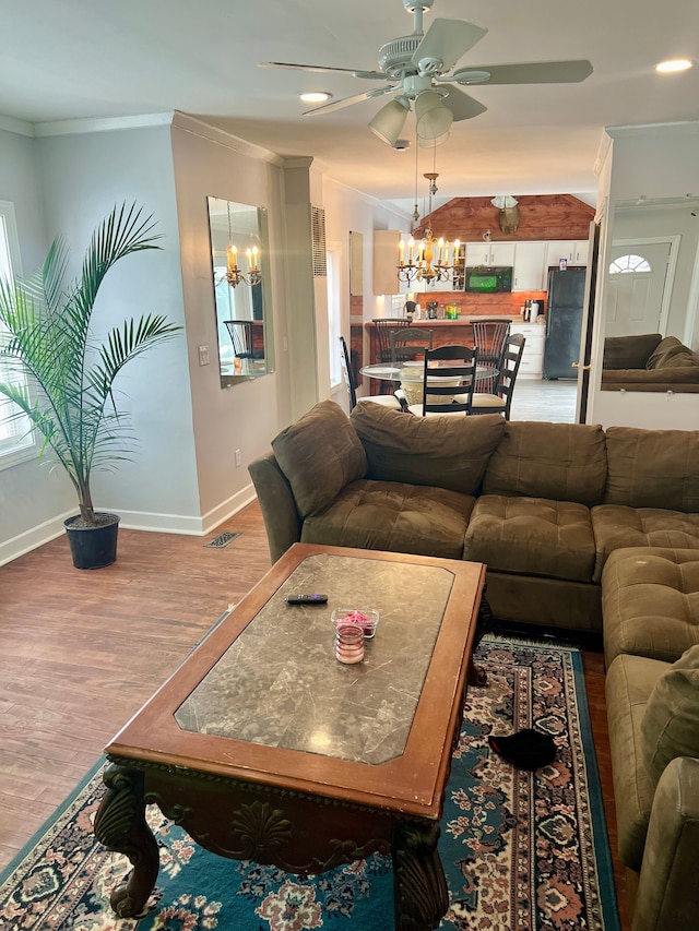 living room featuring wood-type flooring, ceiling fan with notable chandelier, and crown molding