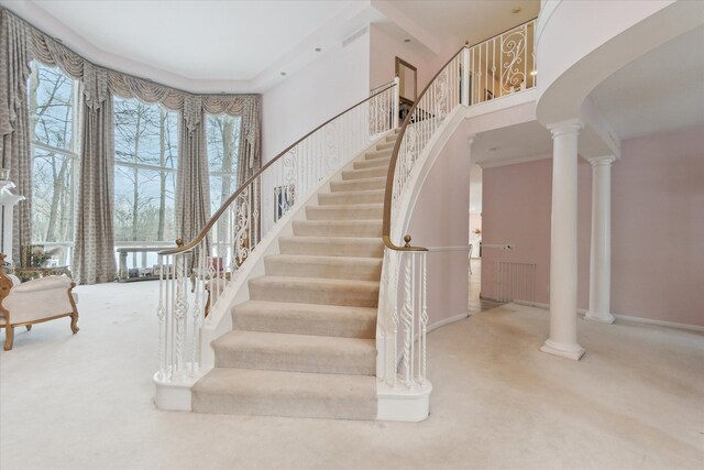 stairs featuring carpet floors, a towering ceiling, and decorative columns