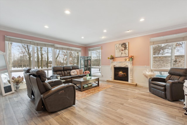 living area featuring a high end fireplace, plenty of natural light, crown molding, and light wood finished floors