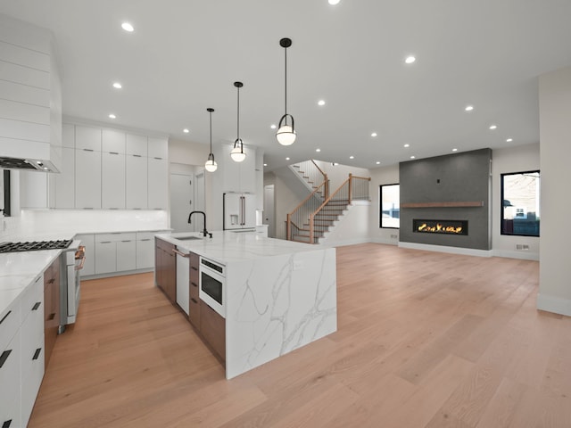 kitchen with light stone countertops, high end appliances, pendant lighting, white cabinets, and a large island