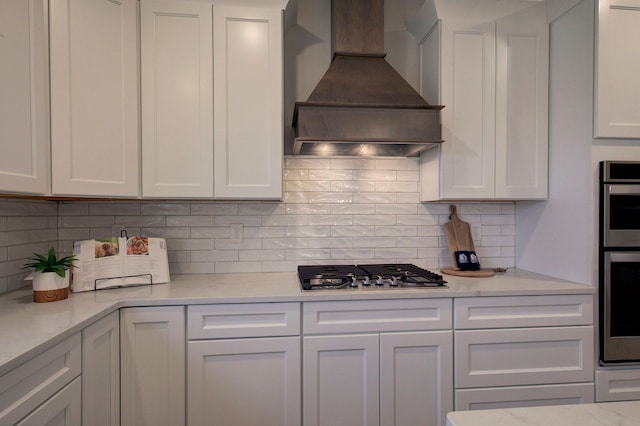 kitchen featuring white cabinetry, light stone counters, custom range hood, and tasteful backsplash