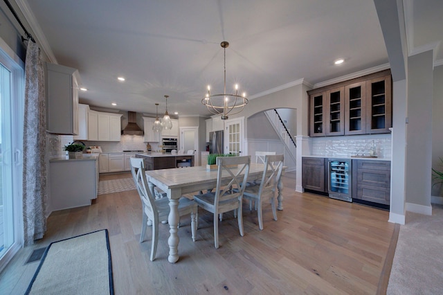 dining space with light hardwood / wood-style floors, crown molding, beverage cooler, and a notable chandelier