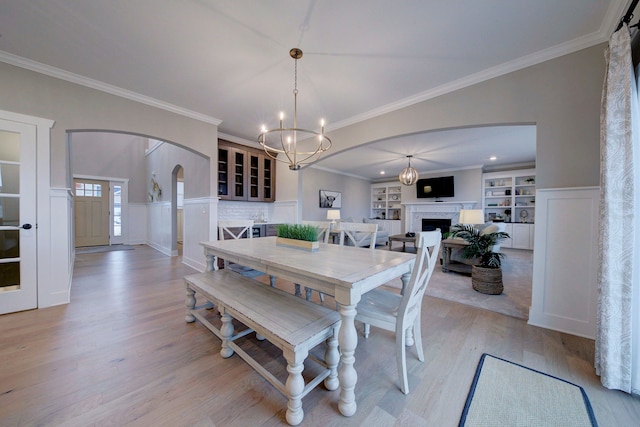 dining space with a chandelier, built in features, ornamental molding, and light wood-type flooring