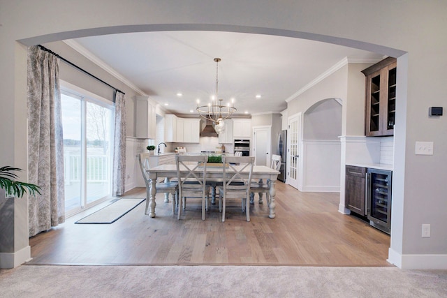 dining room featuring a chandelier, light carpet, wine cooler, and ornamental molding