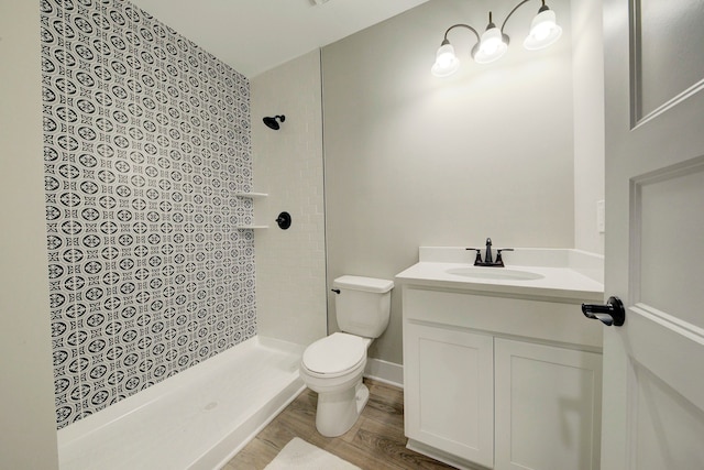 bathroom featuring a tile shower, vanity, wood-type flooring, and toilet