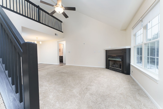 unfurnished living room with high vaulted ceiling, ceiling fan with notable chandelier, light carpet, and a wealth of natural light