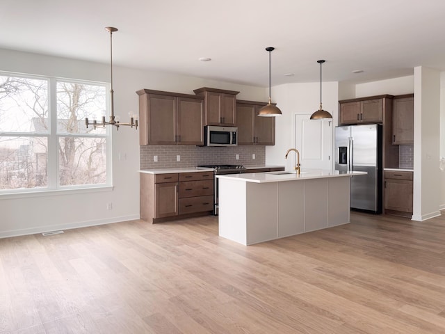 kitchen with appliances with stainless steel finishes, sink, hanging light fixtures, a kitchen island with sink, and light wood-type flooring