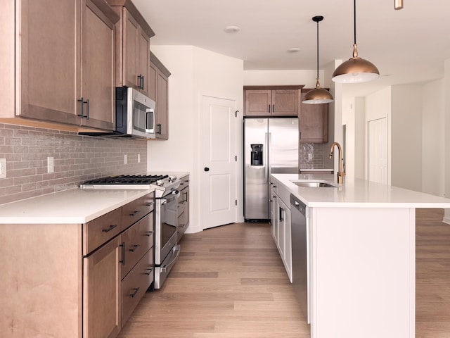 kitchen with sink, a center island with sink, appliances with stainless steel finishes, pendant lighting, and light hardwood / wood-style floors