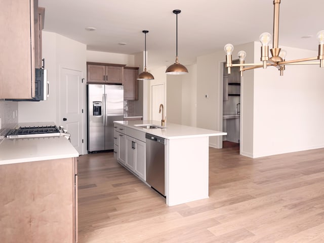 kitchen featuring sink, appliances with stainless steel finishes, a kitchen island with sink, hanging light fixtures, and light hardwood / wood-style floors