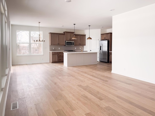 kitchen with hanging light fixtures, backsplash, stainless steel appliances, and an island with sink