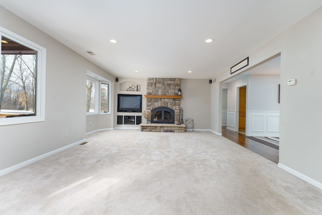 unfurnished living room with a stone fireplace and light colored carpet