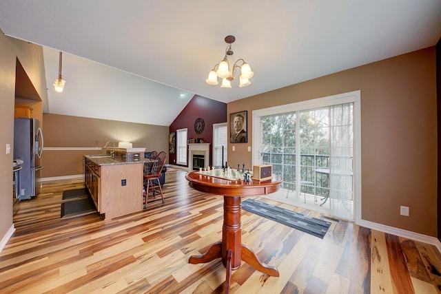 dining space featuring an inviting chandelier, light wood-type flooring, sink, and vaulted ceiling