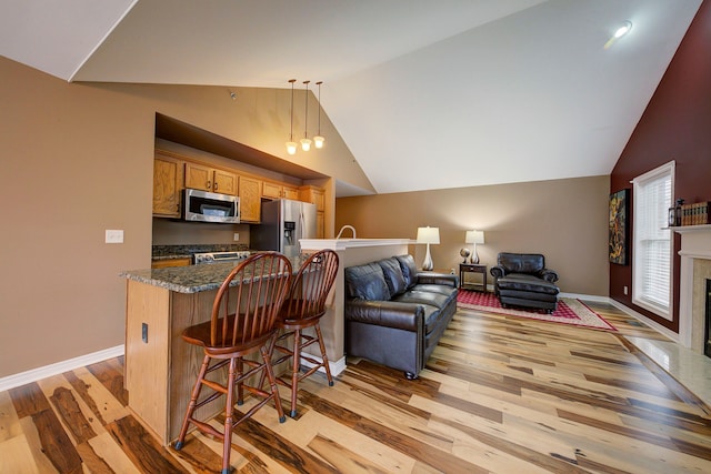 kitchen with light hardwood / wood-style flooring, lofted ceiling, decorative light fixtures, a breakfast bar, and appliances with stainless steel finishes