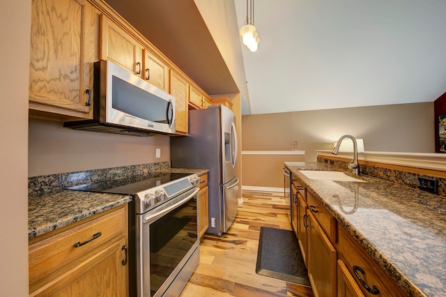 kitchen with hanging light fixtures, sink, dark stone countertops, light wood-type flooring, and appliances with stainless steel finishes