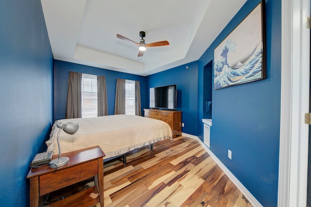 bedroom featuring hardwood / wood-style floors, a raised ceiling, and ceiling fan