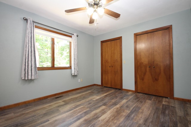 unfurnished bedroom with ceiling fan, dark hardwood / wood-style flooring, and multiple closets