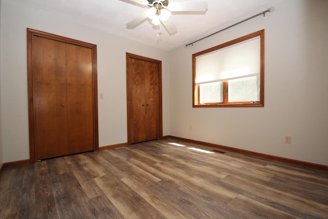 unfurnished bedroom with ceiling fan, dark wood-type flooring, and two closets