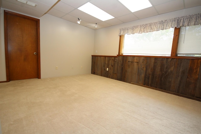 carpeted spare room featuring a paneled ceiling and wood walls