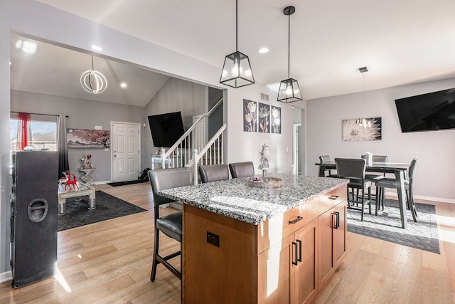 kitchen featuring light stone counters, vaulted ceiling, pendant lighting, and a breakfast bar area