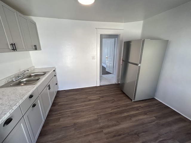 kitchen with white cabinetry, sink, light stone countertops, dark wood-type flooring, and stainless steel fridge