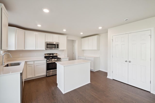 kitchen with appliances with stainless steel finishes, white cabinetry, sink, dark hardwood / wood-style flooring, and a center island