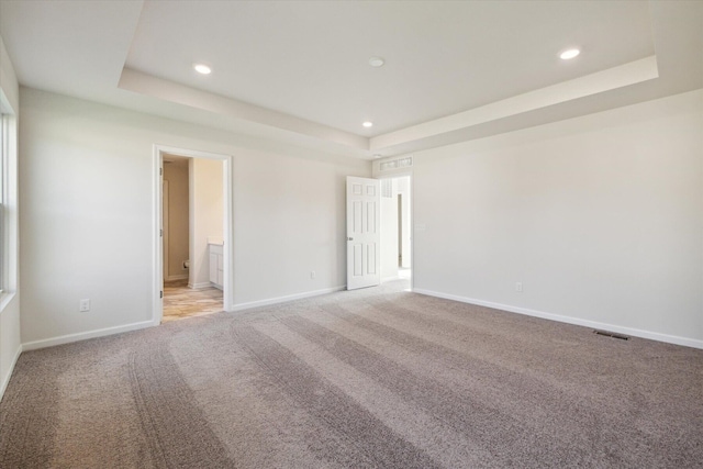 unfurnished bedroom with light colored carpet and a tray ceiling