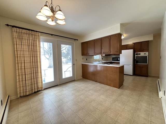 kitchen with decorative light fixtures, oven, white refrigerator, a baseboard heating unit, and kitchen peninsula