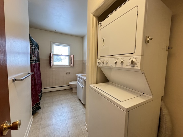 washroom with stacked washing maching and dryer, tile walls, and baseboard heating