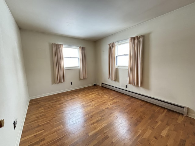 empty room with hardwood / wood-style floors, a baseboard radiator, and a healthy amount of sunlight