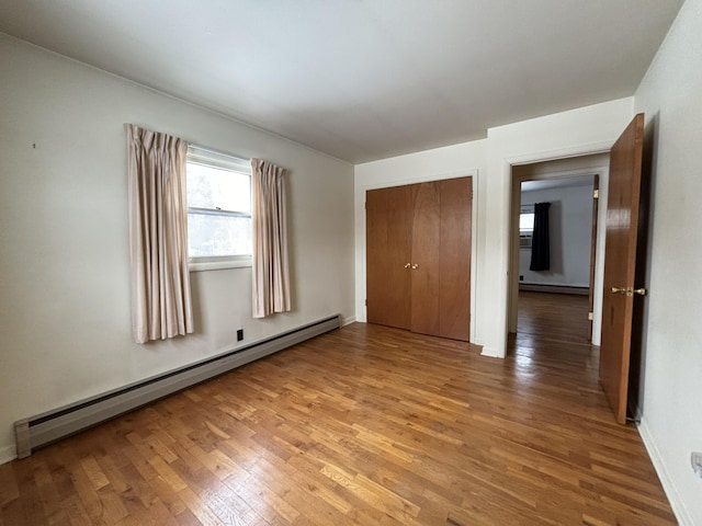 unfurnished bedroom featuring a baseboard heating unit, hardwood / wood-style floors, and a closet