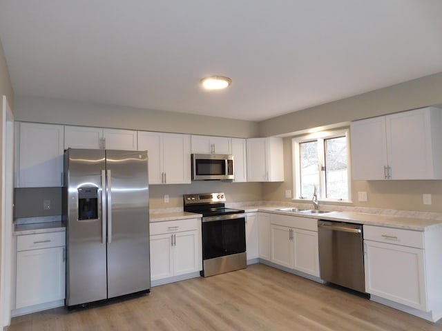 kitchen with white cabinets, stainless steel appliances, light hardwood / wood-style flooring, and sink