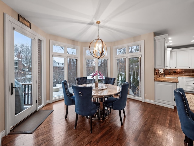 dining area with sink, dark wood-type flooring, and an inviting chandelier