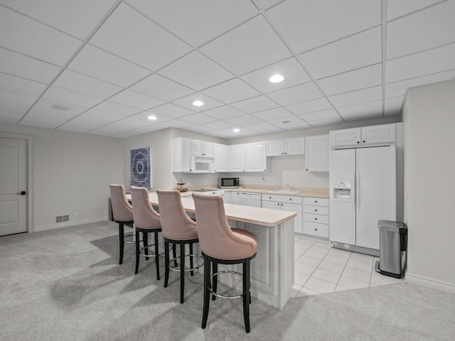 kitchen with white appliances, white cabinets, light colored carpet, sink, and a kitchen bar