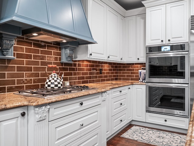 kitchen featuring white cabinetry, light stone countertops, tasteful backsplash, premium range hood, and appliances with stainless steel finishes