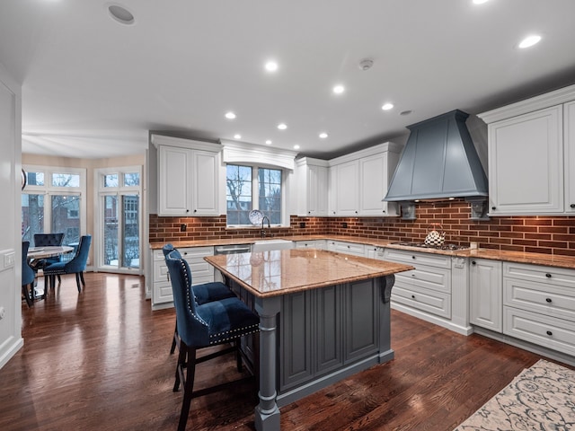 kitchen featuring white cabinetry, light stone counters, a kitchen island, dark hardwood / wood-style flooring, and custom range hood