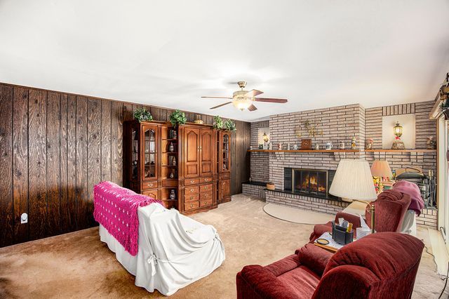 living room featuring a brick fireplace, wooden walls, light colored carpet, and ceiling fan