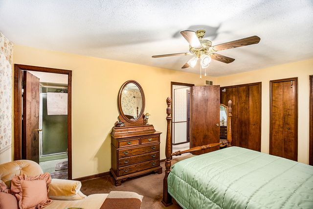 carpeted bedroom with ceiling fan, two closets, ensuite bath, and a textured ceiling