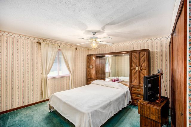 bedroom featuring ceiling fan, dark carpet, and a textured ceiling