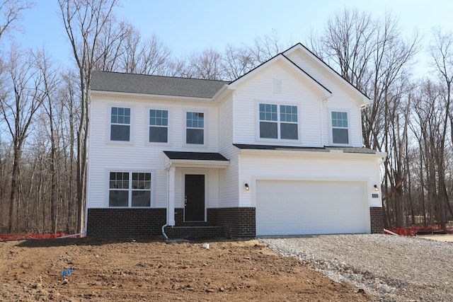 traditional home with gravel driveway, an attached garage, and brick siding